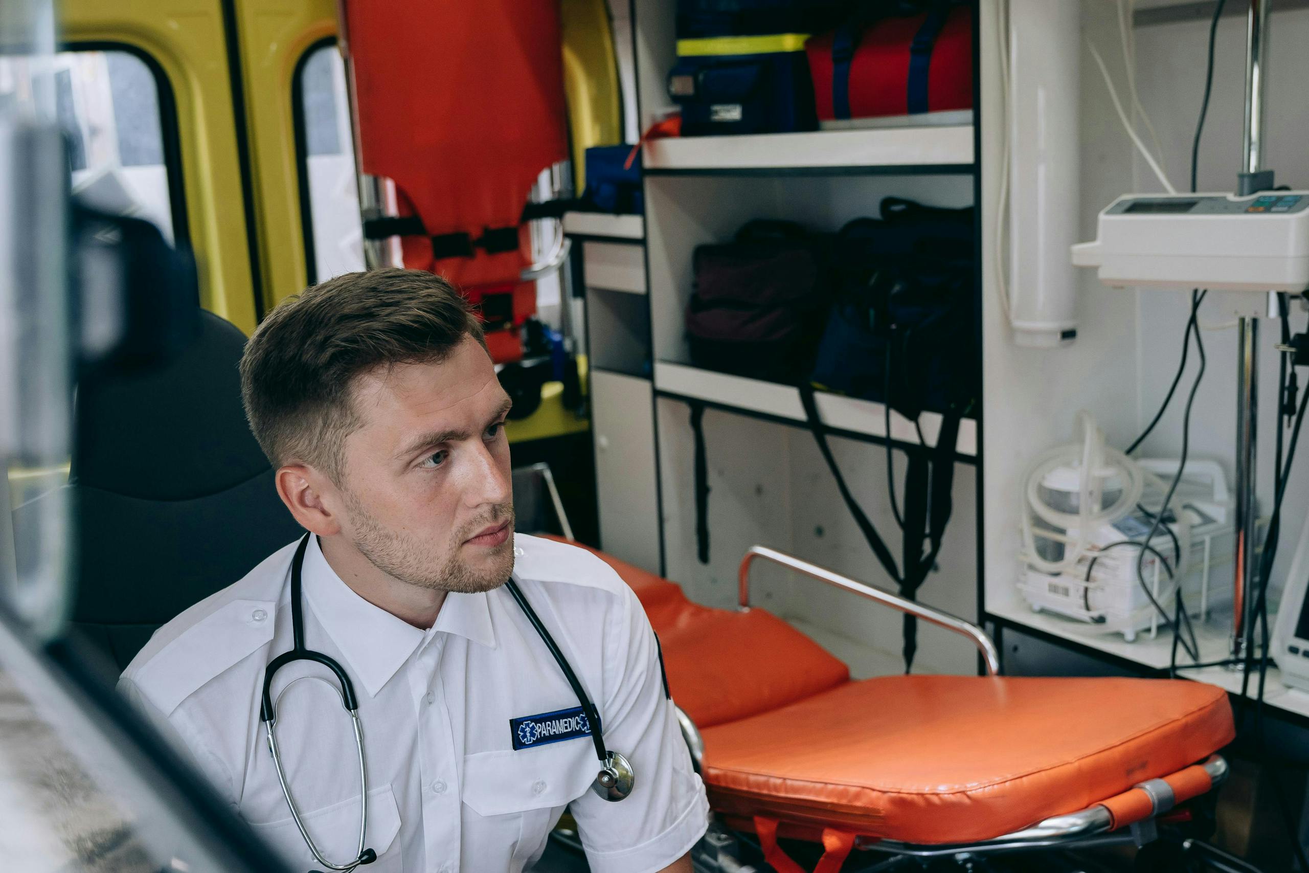 A paramedic with a stethoscope sits inside an ambulance surrounded by medical equipment.