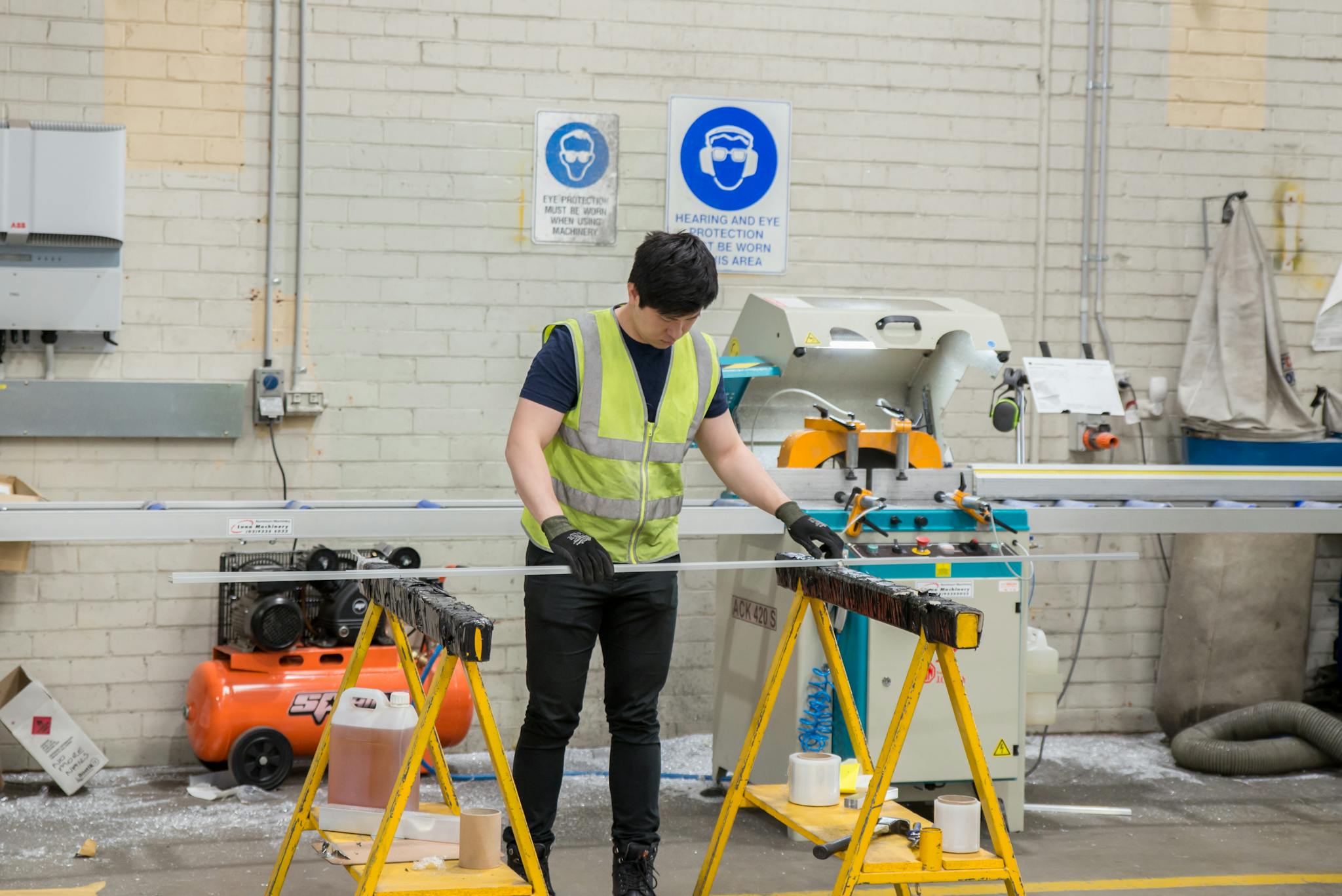 A worker wearing safety gear handling metal bars in a factory setting.