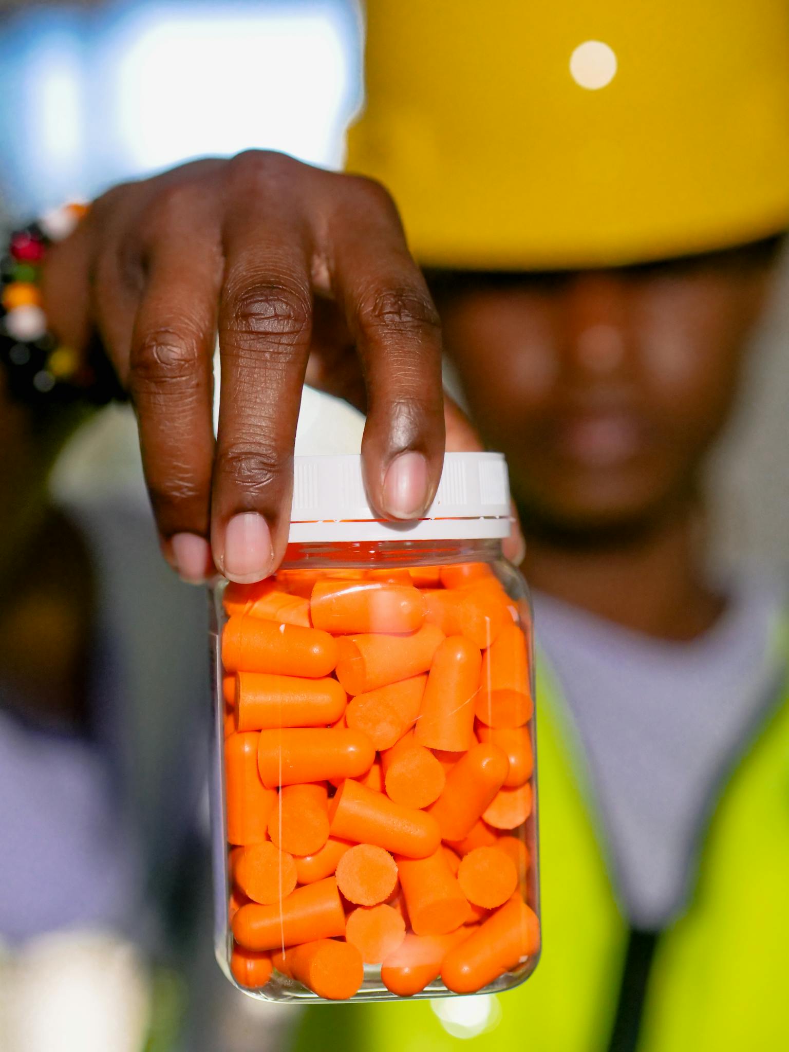 Close-up of a worker holding a jar filled with orange earplugs, focusing on personal protective equipment.
