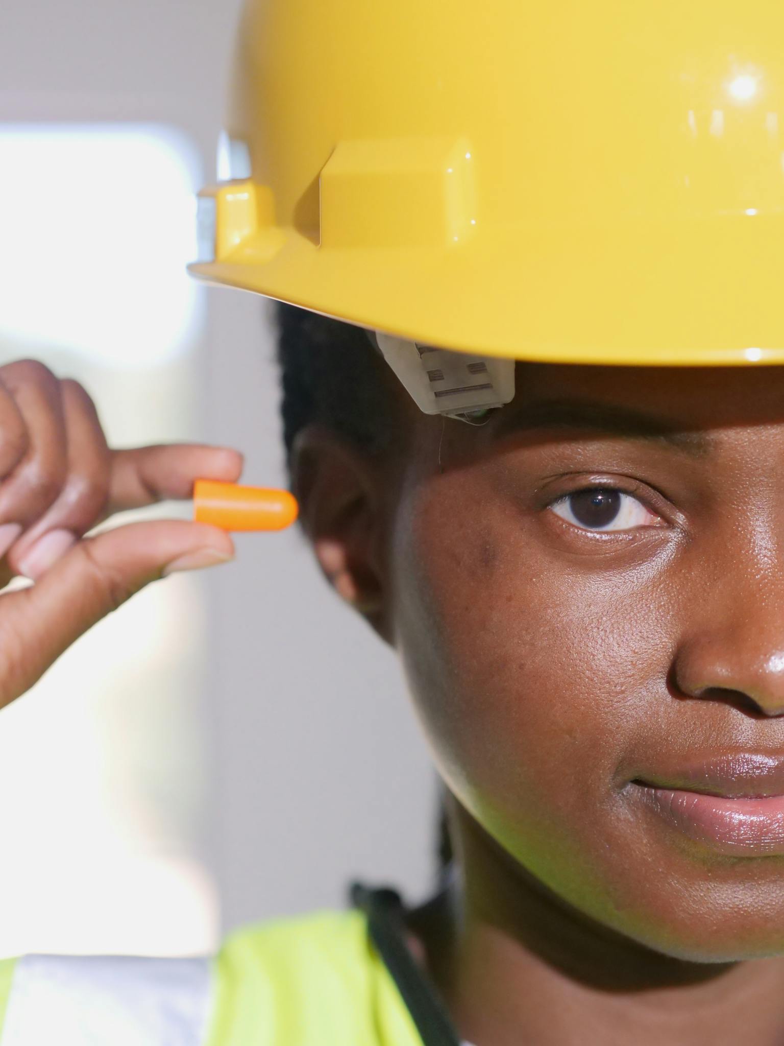 Close-up shot of a woman in a hard hat holding an earplug as personal protective equipment.