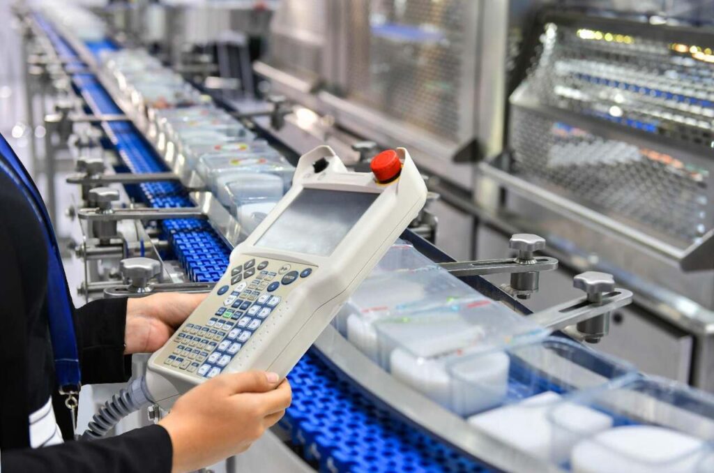 Zdjęcie przedstawia nowoczesną linię produkcyjną w zakładzie przemysłowym, uwzględniającą wymagania bhp i bezpieczne użytkowanie maszyn