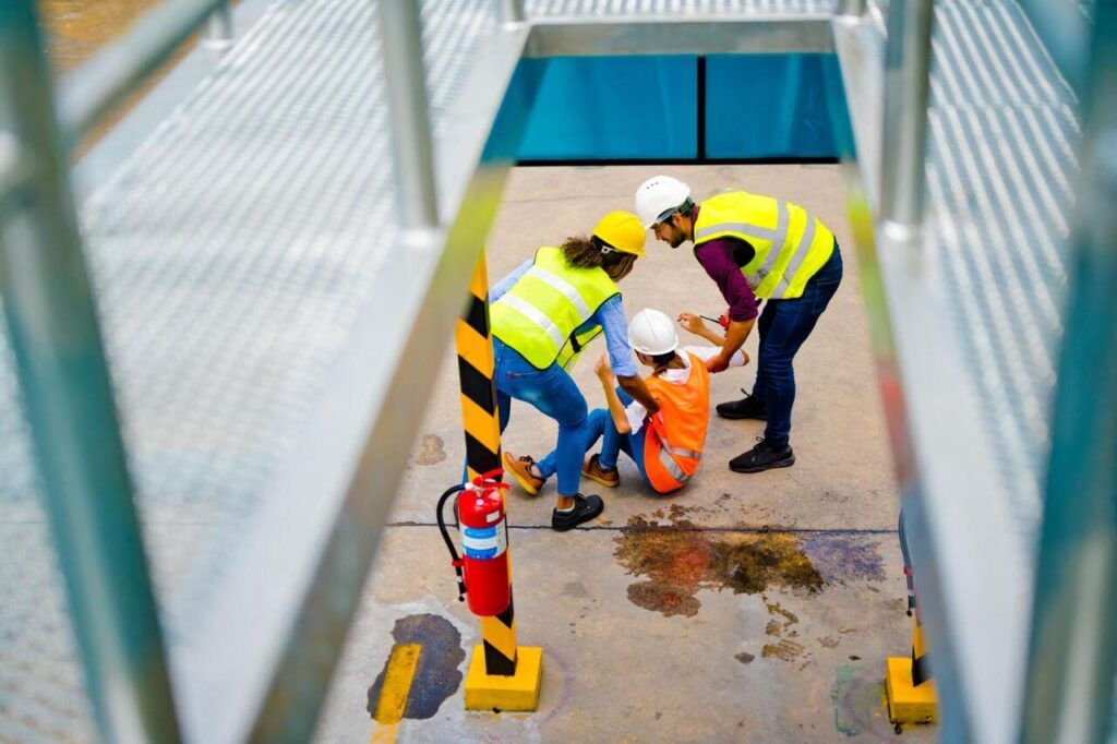 pracownicy udzielają pomocy poszkodowanemu po wypadku przy pracy w zakładzie bhp